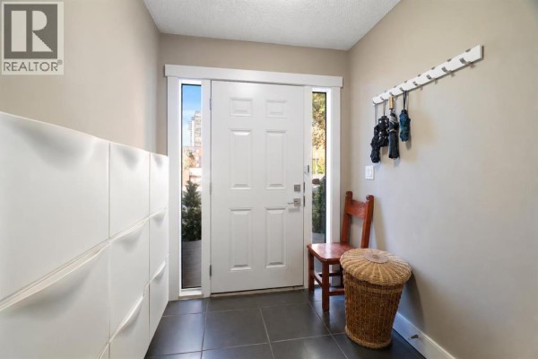 Foyer with a white door, grey tiled floor, and white wall-mounted storage units. - 12, 1339 14 Avenue Sw, Calgary
