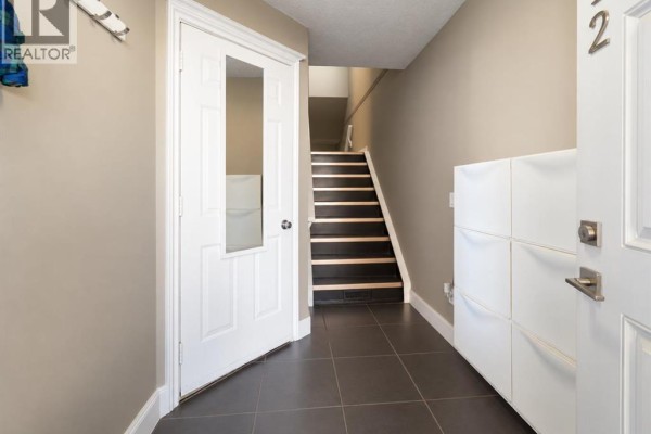 Interior view of a hallway with a white door, staircase with dark treads, and tiled floor. - 12, 1339 14 Avenue Sw, Calgary