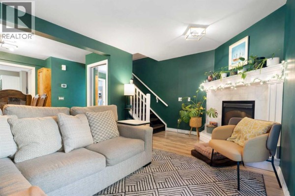 Living room with dark green walls, sectional sofa, armchair, fireplace, and staircase visible. - 12, 1339 14 Avenue Sw, Calgary