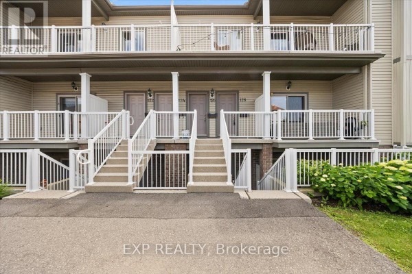 Front entrance of an apartment building with beige siding, white railings, and multiple stairs leading to doors. - 12 - 128 Sternes Private, Ottawa