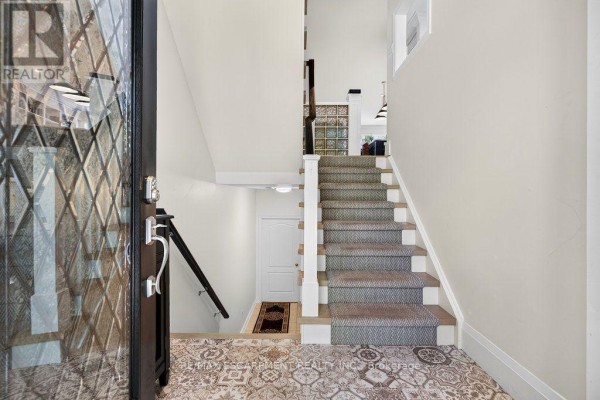 Interior view of a townhouse foyer with a carpeted staircase and patterned tile flooring. - 12 - 1335 Ontario Street, Burlington