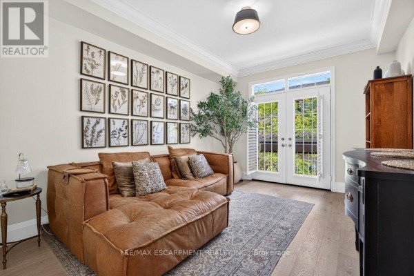 Living room with a large brown leather sectional sofa, botanical prints, and double doors. - 12 - 1335 Ontario Street, Burlington