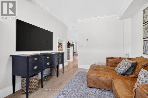 Living room with a black dresser holding a television, and a view into the hallway. - 12 - 1335 Ontario Street, Burlington
