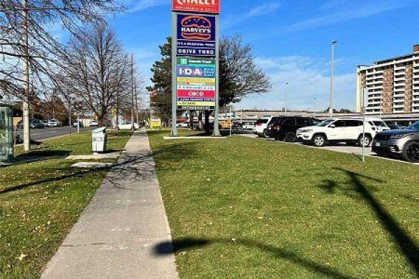 Sidewalk and grassy area with a tall sign listing various businesses including Harvey's and IDA. - 12 - 3237 Bayview Avenue, Toronto