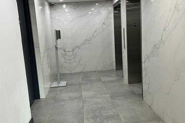 Apartment building hallway with grey tile floors and white marble-patterned walls leading to elevators. - 12 - 3237 Bayview Avenue, Toronto