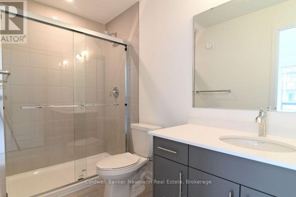 Bathroom with a tiled shower stall, toilet, white vanity with a grey cabinet, and a large mirror. - 12 - 42 Lowes Road W, Guelph