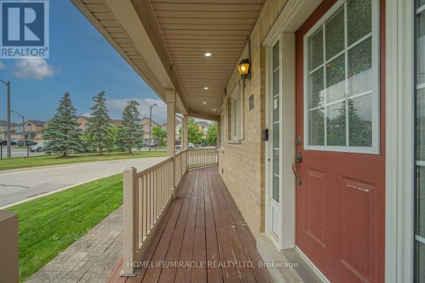 Close-up of a wooden porch with a red front door, doorbell, and light brick exterior. - 12 - 7284 Bellshire Gate, Mississauga