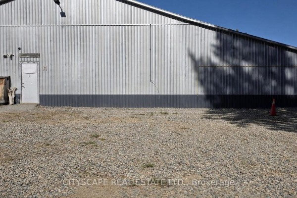 Side view of a corrugated metal commercial building exterior with gravel yard. - 12 - 8021 35 Highway, Kawartha Lakes