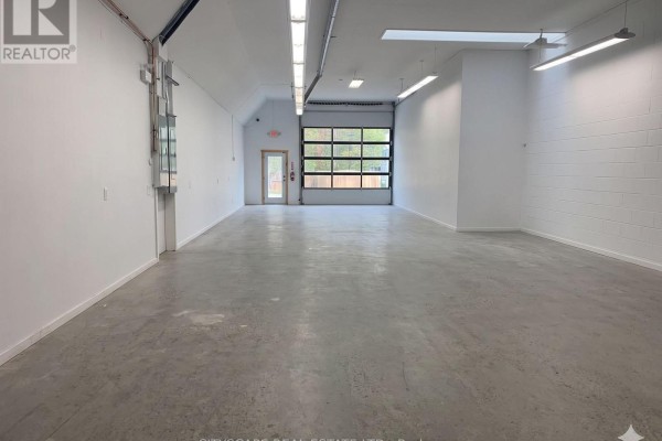 Interior view of a large, empty commercial space with concrete floor and overhead door. - 12 - 8021 35 Highway, Kawartha Lakes