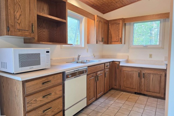 Kitchen featuring oak cabinets, light laminate countertops, a dishwasher, sink, and two windows. - #12 53220 Rge Road 15, Rural Parkland County