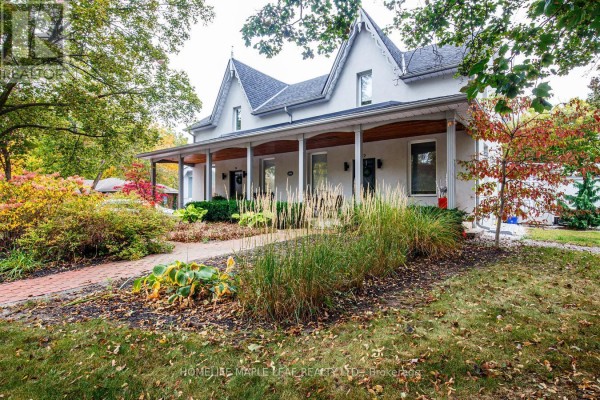 Front exterior of the white house with a covered porch and landscaped garden. - 12 Adamson Street N, Halton Hills