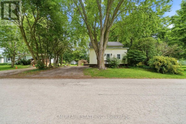 View of a pale yellow house with a small porch from across a gravel driveway. - 12 Argyle Street, Kincardine
