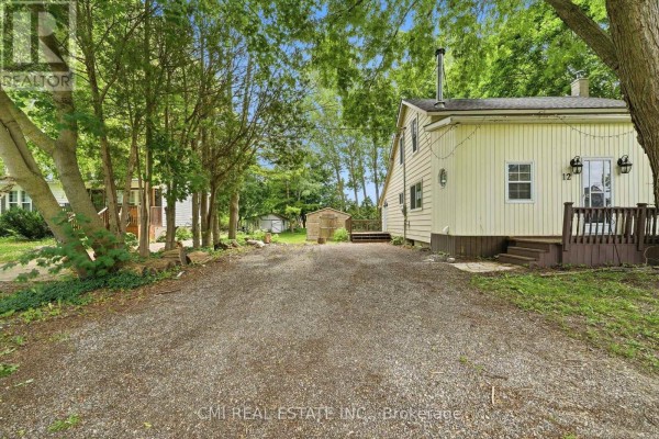 Gravel driveway leading to a pale yellow house with surrounding trees and a shed. - 12 Argyle Street, Kincardine