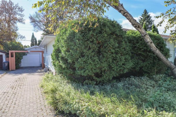 Side view of the house showing a paved driveway leading to a detached garage. - 12 Barberry Road, Winnipeg