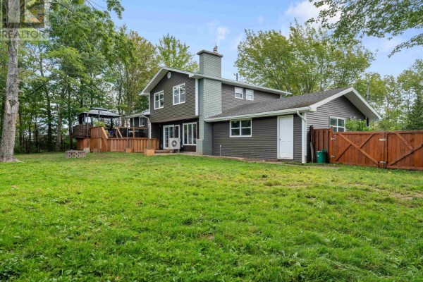Backyard view of the house with a wooden deck, fenced yard, and mature trees. - 12 Birch Hill Drive, Stellarton