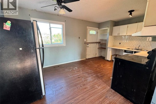 Kitchen area with a black refrigerator, window, white cabinets, and dark wood laminate flooring. - 12 Bowerman Crescent, Prince Albert
