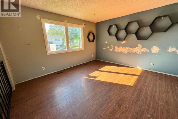 Living room with a large window, dark teal accent wall with hexagonal shelves, and wood laminate flooring. - 12 Bowerman Crescent, Prince Albert
