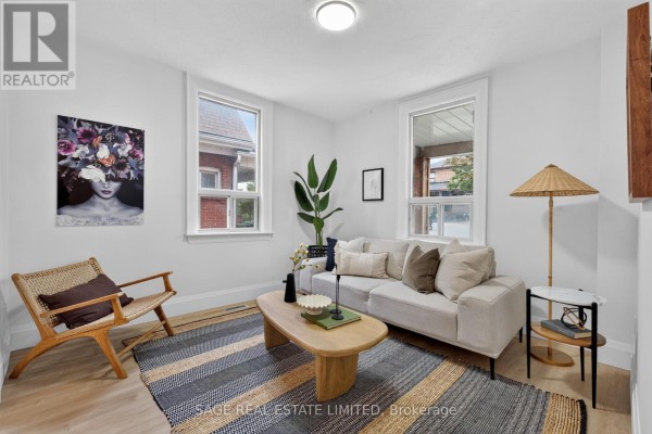 Living room with a beige sofa, wooden coffee table, striped rug, and two windows. - 12 Branstone Road, Toronto