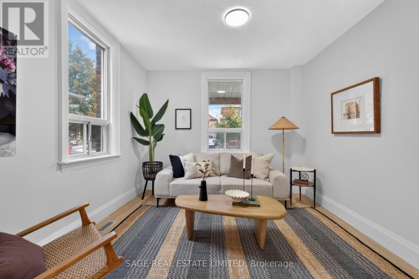 Living room with a sofa, armchair, coffee table, striped rug, and two windows. - 12 Branstone Road, Toronto