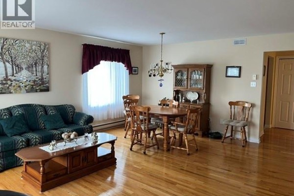 Living and dining room with green patterned sofa, wood dining set, and hardwood floors. - 12 Caitlin Court, Saint John