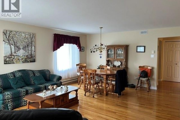 Living and dining area with a sofa, dining table, hutch, and hardwood floors. - 12 Caitlin Court, Saint John