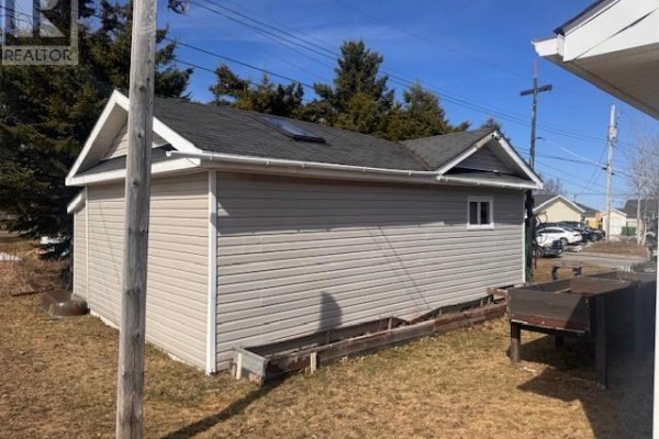 Side view of a detached garage with light grey vinyl siding, a small window, and a black asphalt roof. - 12 Cedar Drive, Lewisporte