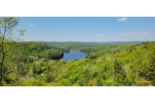 View overlooking a serene blue lake surrounded by rolling hills covered in vibrant green trees. - 12 Ch. Du Mica, Val Des Monts