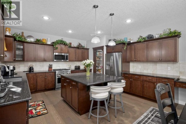 Large kitchen with dark wood cabinets, granite countertops, a central island, and stainless steel appliances. - 12 Crestridge Rise Sw, Calgary