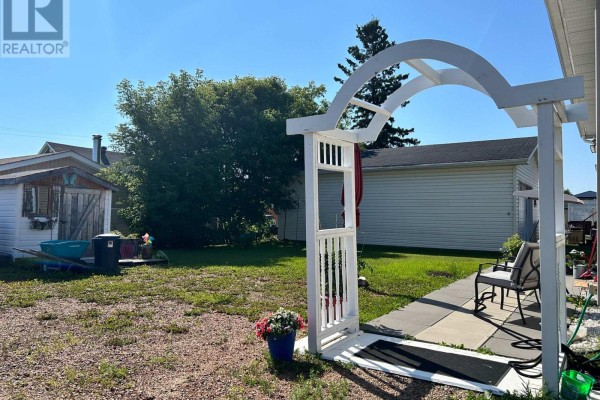 Backyard view with a white archway, patio, shed, and chain-link fence. - 12 Erickson Avenue, Kapuskasing