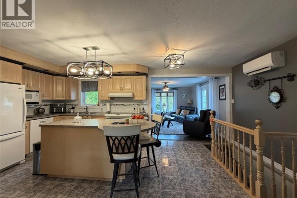 Kitchen with light wood cabinets, an island with bar stools, and an adjoining living room. - 12 Eugène Street, Saint Basile