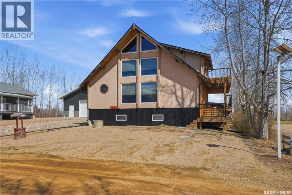 Side view of a beige house with a wooden deck and railing, next to a tall metal pole. - 12 Finch Crescent, Thomson Lake