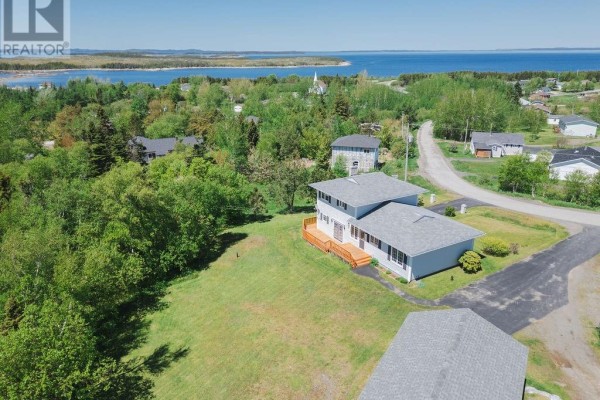 Aerial view of a light grey house with wooden deck overlooking a bay. - 12 Hancott's Lane, Frederickton