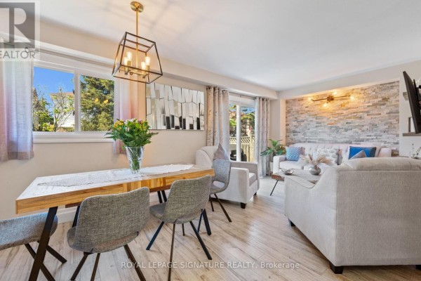 Dining area with a wooden table and grey chairs, adjacent to a living room with a stone accent wall. - 12 Hewitt Crescent, Ajax