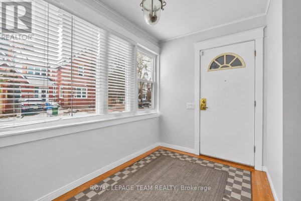 Entryway with white door, arched window, checkered floor mat, and large windows overlooking the street. - 12 Lewis Street, Ottawa
