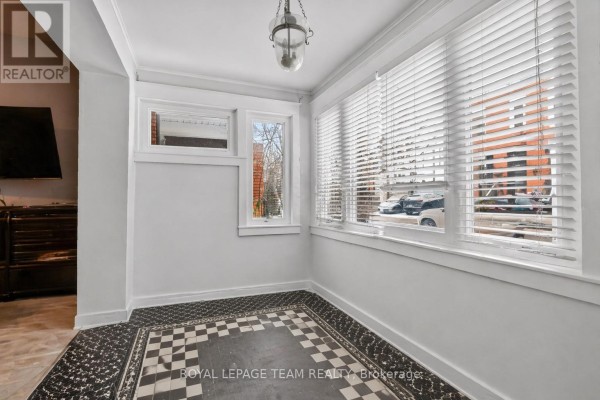 Bright sunroom with checkered floor, white blinds on windows, and views of the street and neighboring buildings. - 12 Lewis Street, Ottawa