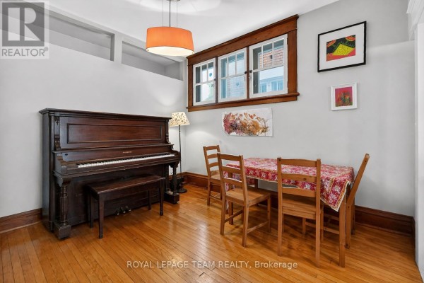 Dining area with wooden table and chairs next to an upright piano, hardwood floors, and window views. - 12 Lewis Street, Ottawa