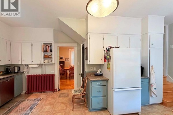 Kitchen with white cabinets, teal lower cabinets, a red radiator, a white refrigerator, and a doorway to a dining area. - 12 Matheson Avenue, Edmundston