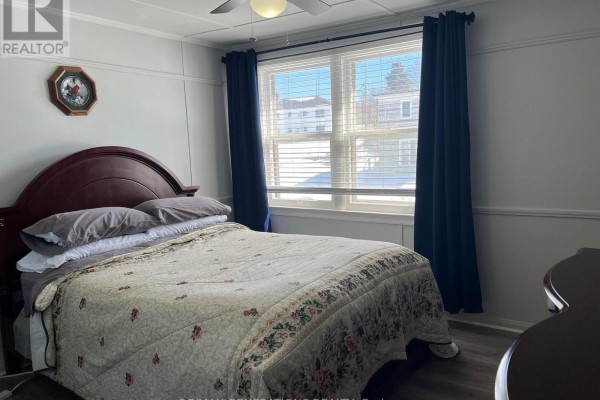 Bedroom with a queen-size bed, dark wood headboard, and a window with blue curtains. - 12 Mccullough Street, Marathon