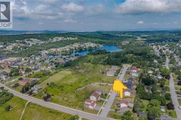 Aerial view showcasing the vacant lot on Mosaic Drive with houses and a distant lake. - 12 Mosaic Drive, Saint John