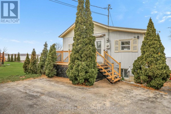 Side view of the house with wooden stairs leading to a deck and tall evergreen trees lining the property. - 12 Robins Point Road, Tay