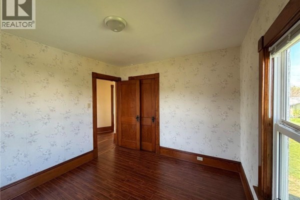 Bedroom with floral wallpaper, hardwood floors, and a double wooden door leading to another room. - 12 Sc Breakwater, Grand Manan