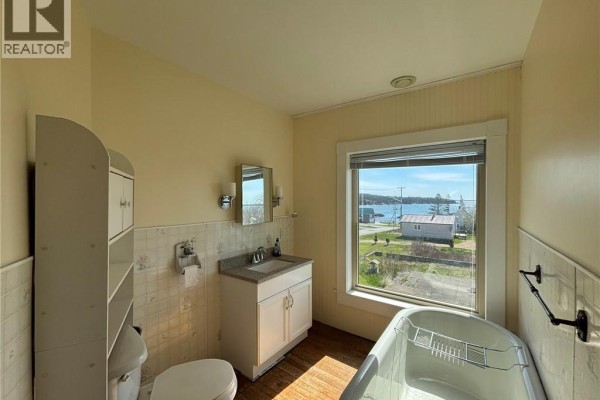 Bathroom with a tub, toilet, vanity, and a window overlooking a coastal village and harbor. - 12 Sc Breakwater, Grand Manan