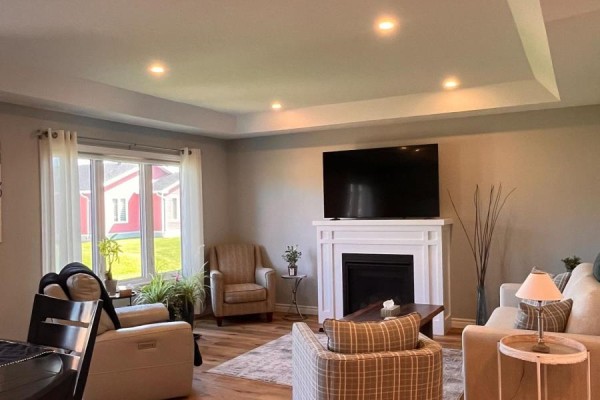 Living room with a fireplace, large television, and neutral-toned furniture. - 12 Sweetwater Drive S, Goderich)