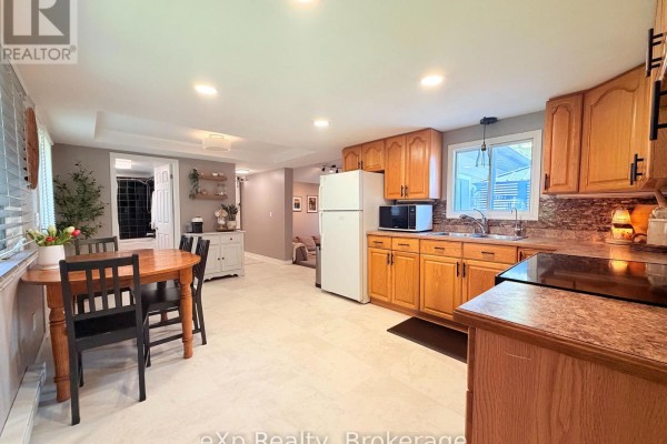 Open-concept kitchen and dining area with light wood cabinets, beige tiled floors, and a wooden dining set. - 12 Union Street N, Brockton