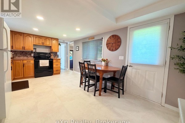 Kitchen and dining area showing oak cabinets, black appliances, beige tile floor, and a white door to the outside. - 12 Union Street N, Brockton