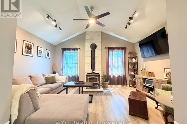 Living room with a vaulted ceiling, grey sectional sofa, stone fireplace with wood stove, and a large ceiling fan. - 12 Union Street N, Brockton
