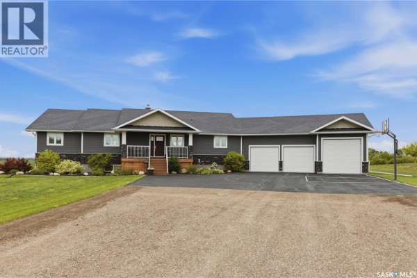 Front exterior of a dark grey residential house with a white-railed front porch and a three-car garage. - 12 Valley Ridge Road, Last Mountain Lake