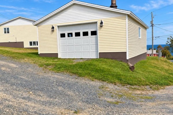 Detached yellow garage with a white overhead door and window panes. - 12 Welsh's Lane, Pouch Cove
