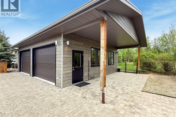 Exterior of house with wood siding, stone base, and paved patio area. - 12/14 Bruin Boulevard, Candle Lake