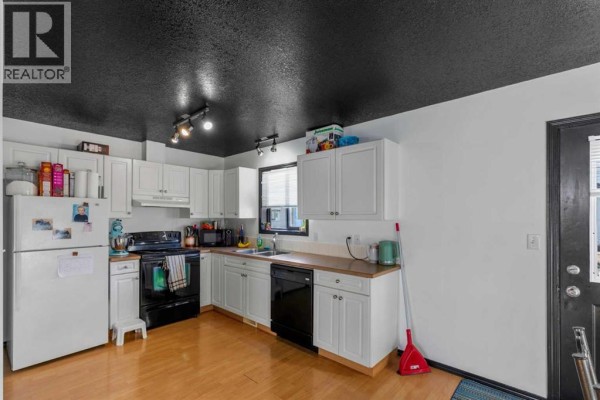 A compact kitchen with white cabinets, black appliances, and a dark textured ceiling. - 120, 10150 121 Avenue, Grande Prairie